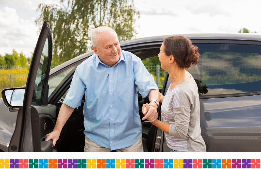 A woman is helping an older man get out of a car. They are both happy he is home.