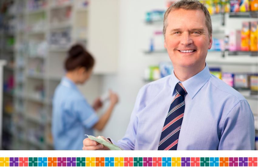Male pharmacist smiling at camera holding prescription